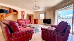 A living room with red leather sofas, a coffee table, a TV, and a staircase.