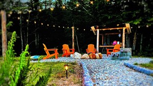 A rustic outdoor seating area with wooden chairs and a table, surrounded by rocks and greenery. - Cozy Cabin with Outdoor Shower, Fireplace, Games, Firepit and a Mountain View! (Campton)