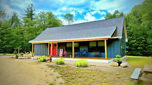A single-story building with a porch, a red door, and a covered outdoor seating area. - Cozy Cabin with Outdoor Shower, Fireplace, Games, Firepit and a Mountain View! (Campton)