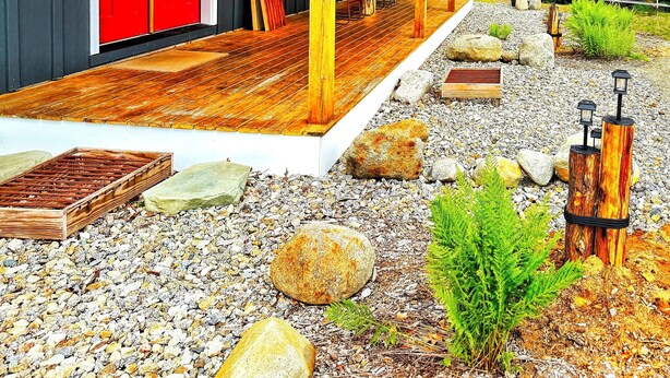 A modern house with a red door, a wooden deck, and a garden with rocks and plants. - Cozy Cabin with Outdoor Shower, Fireplace, Games, Firepit and a Mountain View! (Campton)