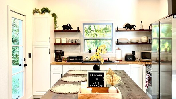 Una cocina moderna con una isla central, muebles blancos y vistas a zonas verdes.