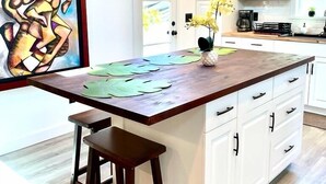 Una cocina con una isla de madera, armarios blancos y un cuadro en la pared.