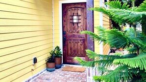 Una casa amarilla con puerta principal de madera, plantas en macetas y un camino de ladrillo que lleva a la puerta.