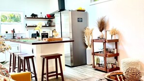 Una cocina moderna con una isla central, una zona de comedor con sofá y sillas, y una sala de estar con un cofre de madera grande.