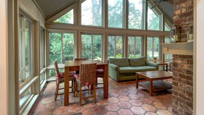A spacious room with large windows, a wooden dining table, wicker chairs, a green sofa, and a brick fireplace. - 8 Ruddy Turnstone at The Sea Pines Resort (Hilton Head Island)