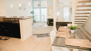 A modern kitchen with a central island, a dining area with a wooden table, and a staircase leading to an upper level.