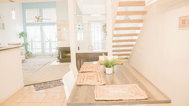 A modern kitchen with a wooden table, white chairs, and a staircase.