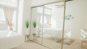 A bedroom with a large mirror, a bed, a bedside table, a chair, and a small table with a lamp.