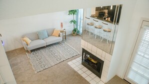 A living room with a sofa, a patterned rug, a fireplace, and a kitchen area with bar stools.