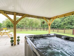 A hot tub under a wooden pergola with a view of a fenced yard and trees. - Talarddu Cottage (Builth Wells)