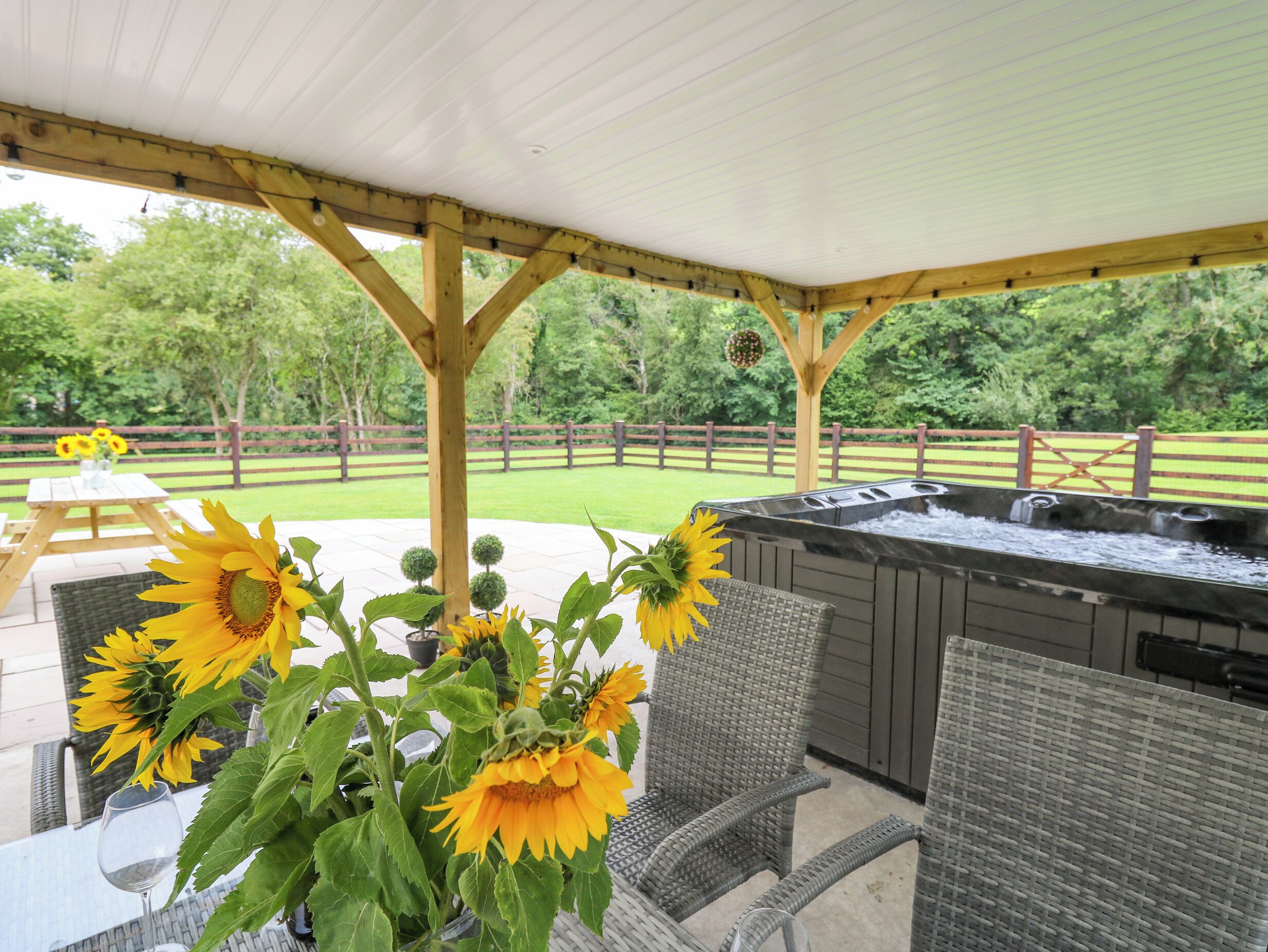 An outdoor patio area with a covered seating area, a hot tub, and sunflowers.