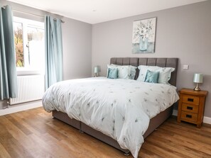 A bedroom with a large bed, two bedside tables, a window with curtains, and a painting on the wall. - Talarddu Cottage (Builth Wells)