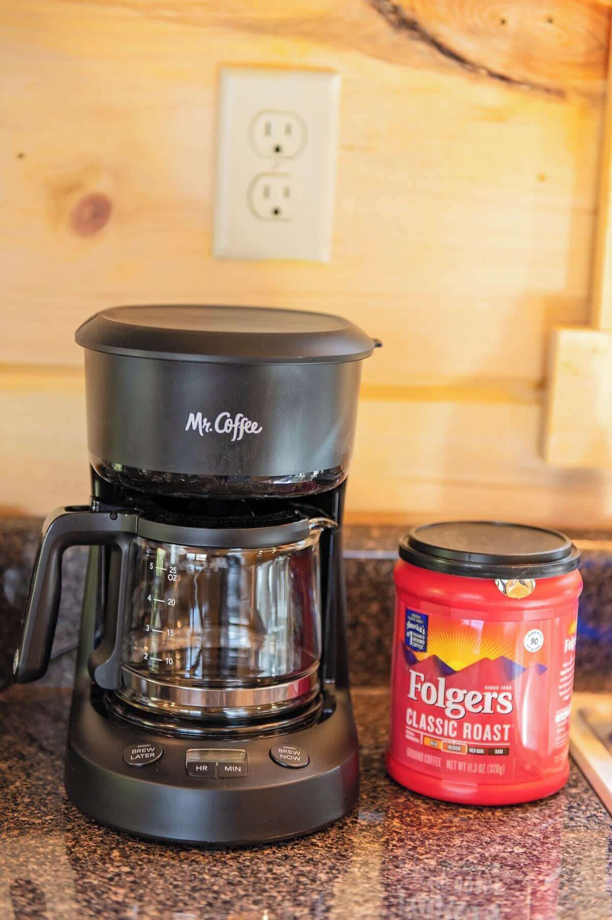 Una cafetera y un bote de café Folgers sobre una encimera de cocina.