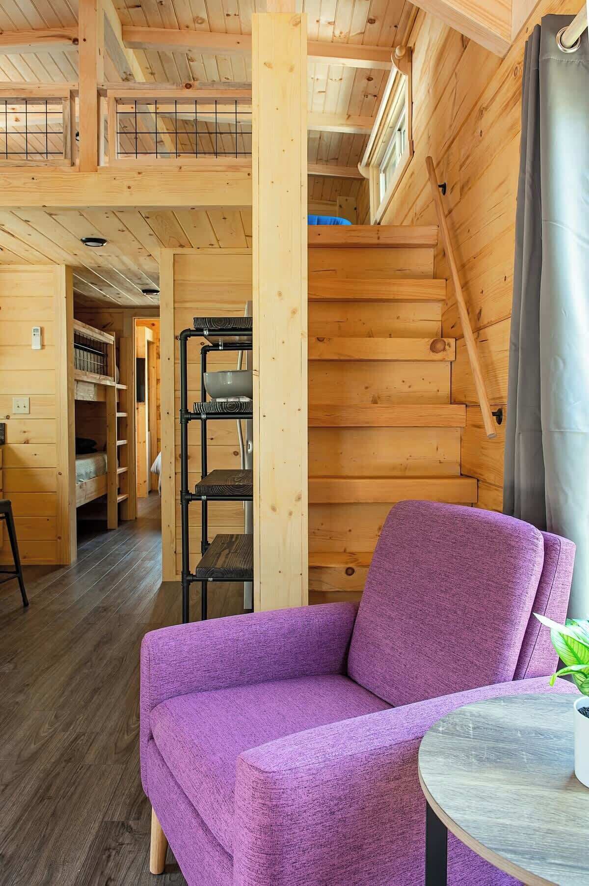 L'intérieur d'un chalet en bois, avec un canapé violet, une petite table et un escalier.