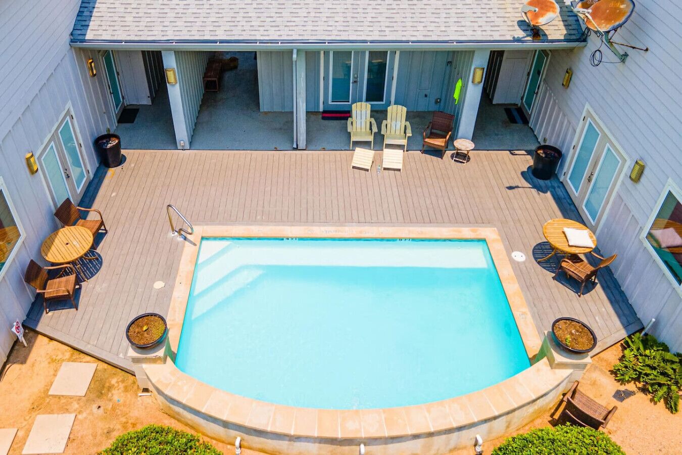 A rectangular swimming pool with a wooden deck surrounding it, equipped with lounge chairs and tables.