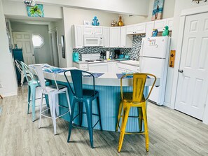 A modern kitchen with white cabinets, a blue island, and a yellow chair.