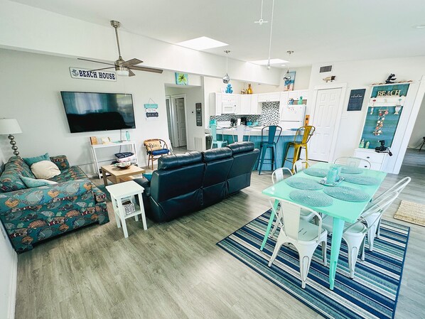 A modern living room with a sofa, a dining table, and a kitchen area.