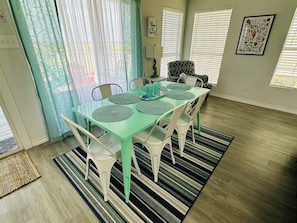 A dining area with a green table, white chairs, and a striped rug.