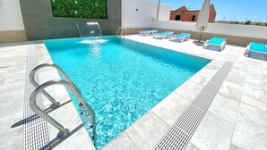 A swimming pool with a clear blue water, a metal ladder, and several lounge chairs with blue cushions. - Hotel Don Pepo (Lobón)
