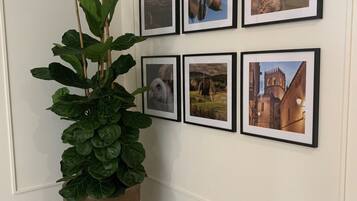 Een gang met een grote potplant, zes ingelijste foto’s aan de muur en een betegelde vloer.