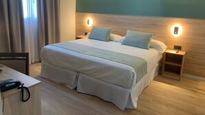 A neatly arranged hotel room with a large bed, bedside tables, a desk with a telephone, and a window with curtains. - Hotel Don Pepo (Lobón)