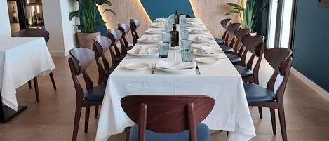 A dining area with a long table set for a meal, surrounded by chairs with cushioned seats.