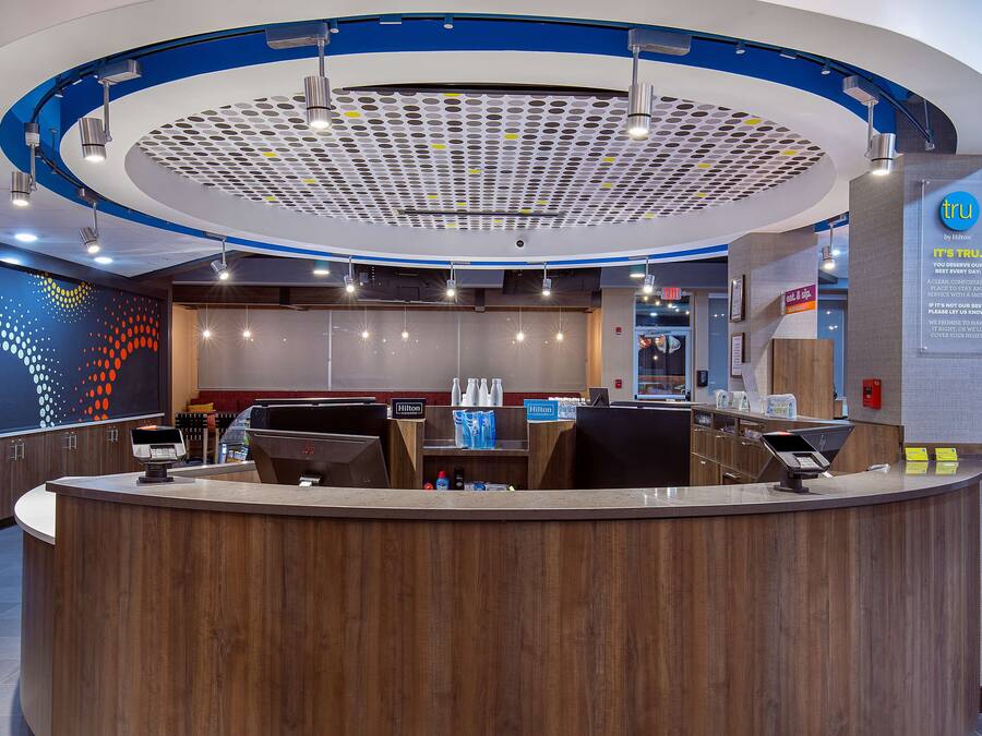 Una moderna zona de recepción de hotel con un mostrador curvo de madera, una pantalla digital y un techo con un diseño perforado único.