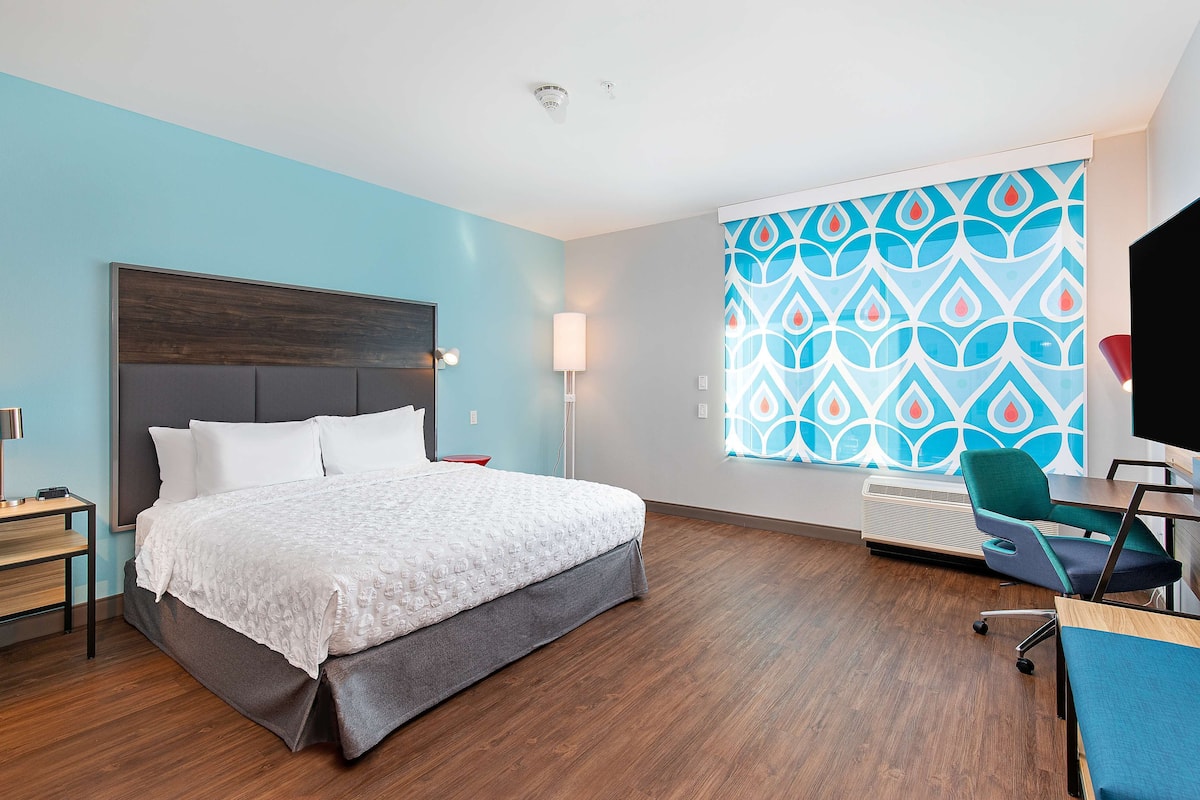 Hotelkamer met een bed, bureau, stoel, televisie en raam met een gordijn met patroon.