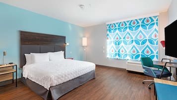Habitación de hotel con cama, escritorio, silla, televisión y ventana con cortina estampada.