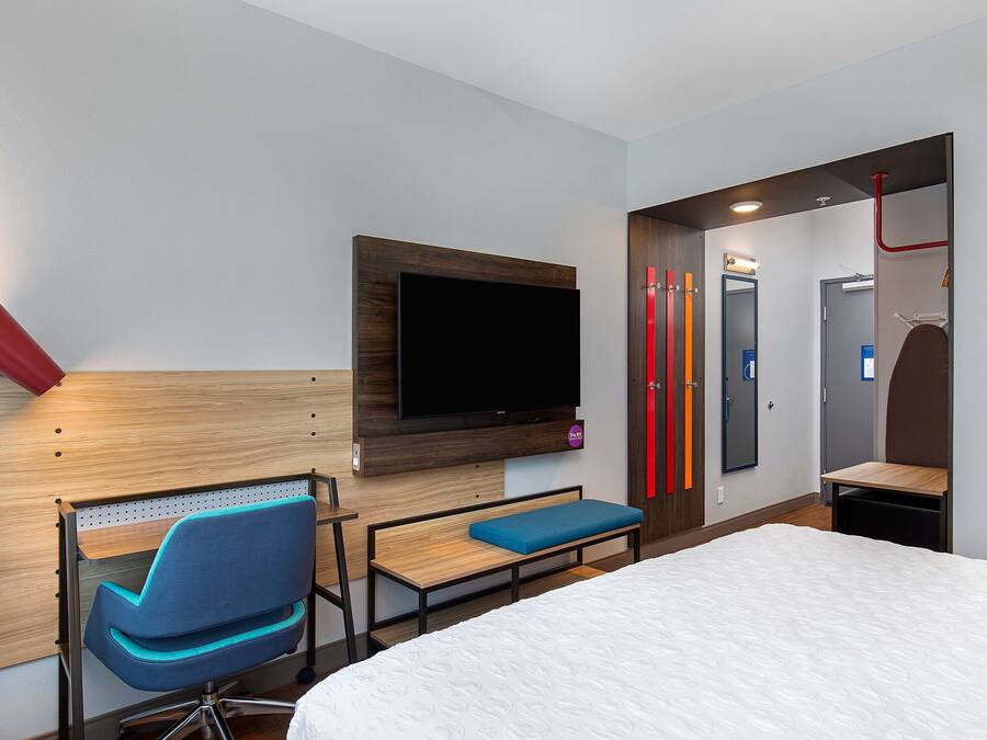 Habitació d'hotel amb llit, escriptori amb cadira, televisió penjada a la paret i bany amb mirall i portes vermelles.