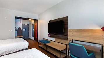 A hotel room with two beds, a desk with a chair, a TV mounted on the wall, and a door leading to a bathroom.
