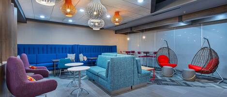 Un espace lounge moderne avec différents types de sièges, notamment un canapé bleu, des fauteuils violets et un fauteuil suspendu rouge.