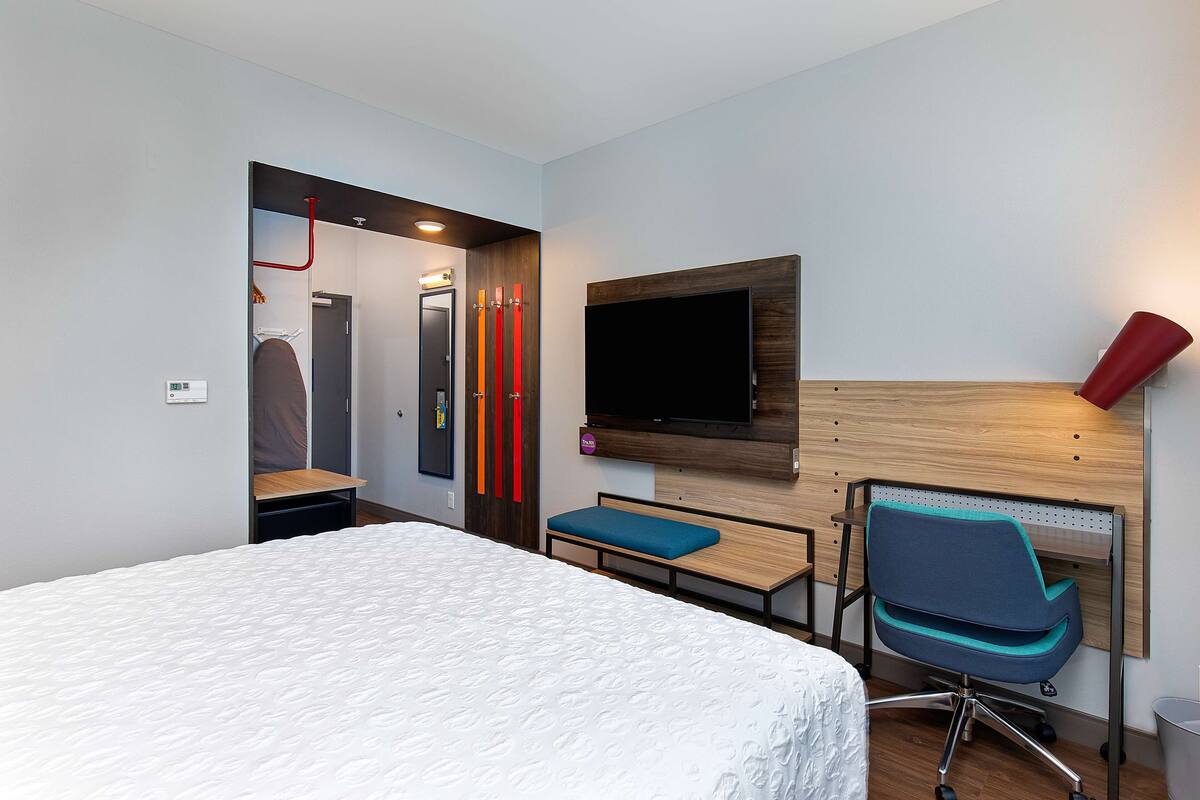 Een hotelkamer met een bed, een bureau met stoel, een aan de muur bevestigde televisie en een rode lamp.