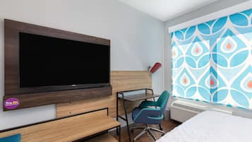 Een hotelkamer met een aan de muur bevestigde televisie, een bureau met stoel en een bed met een wit dekbed.