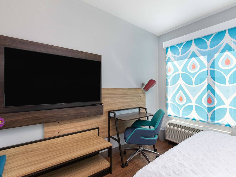 Een hotelkamer met een aan de muur bevestigde televisie, een bureau met stoel en een bed met een wit dekbed.