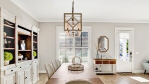 A dining room with a wooden table, white cabinets, and a chandelier. - Coastal Luxury Cottage | Beach Access | Pet Friendly (Orange Beach)