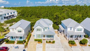 A residential area with modern houses, a paved driveway, and a forested hill in the background. - Coastal Luxury Cottage | Beach Access | Pet Friendly (Orange Beach)