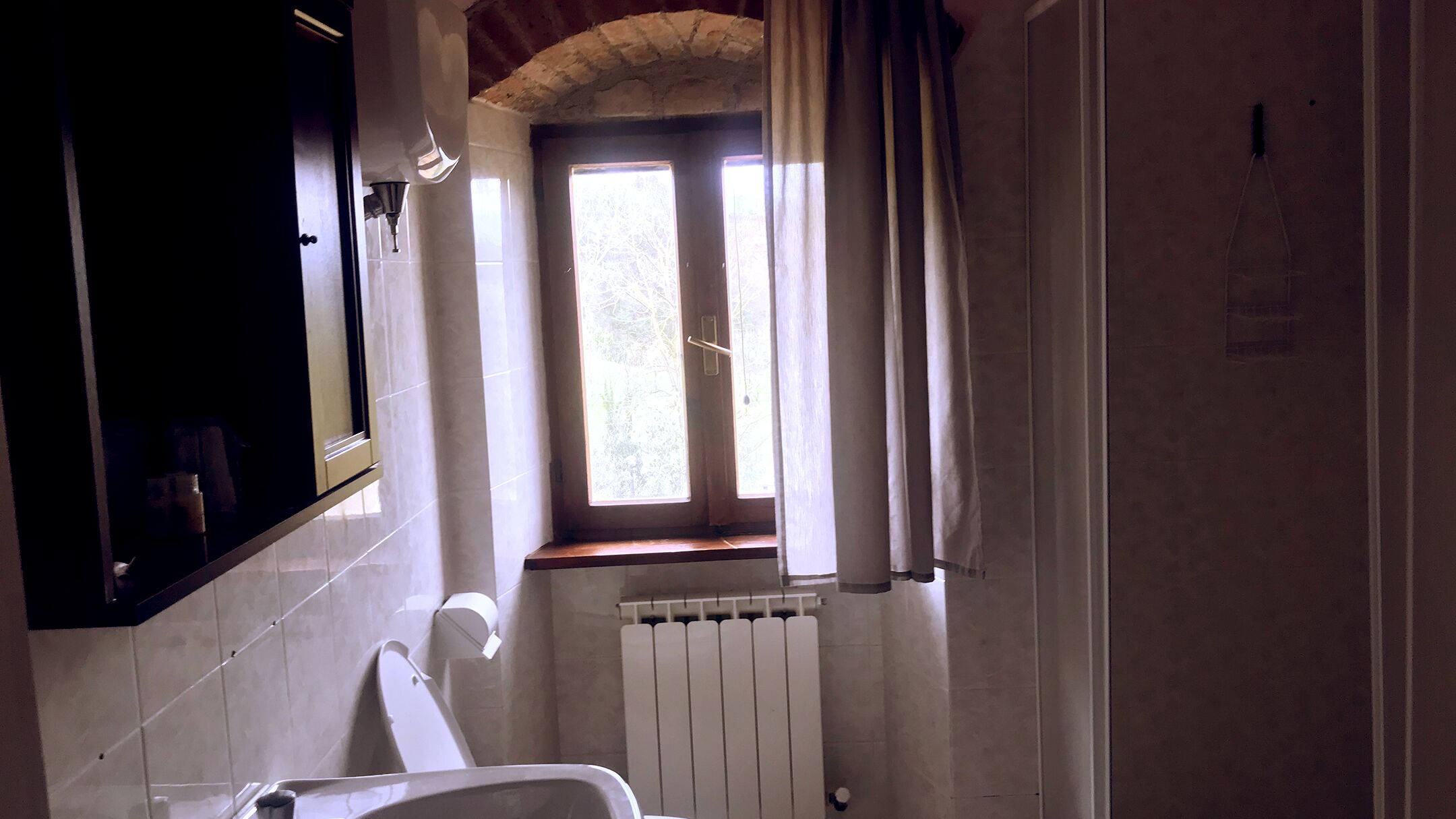 A bathroom with a toilet, a sink, a mirror, and a window with curtains.