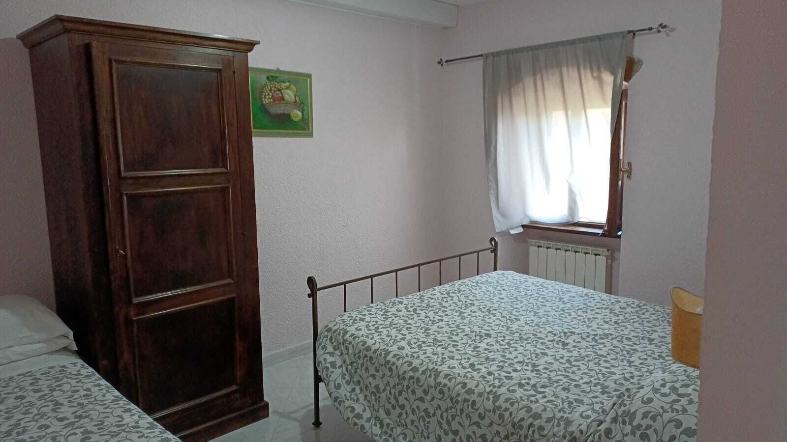 Een slaapkamer met een bed, een kledingkast, een radiator en een raam met gordijnen.