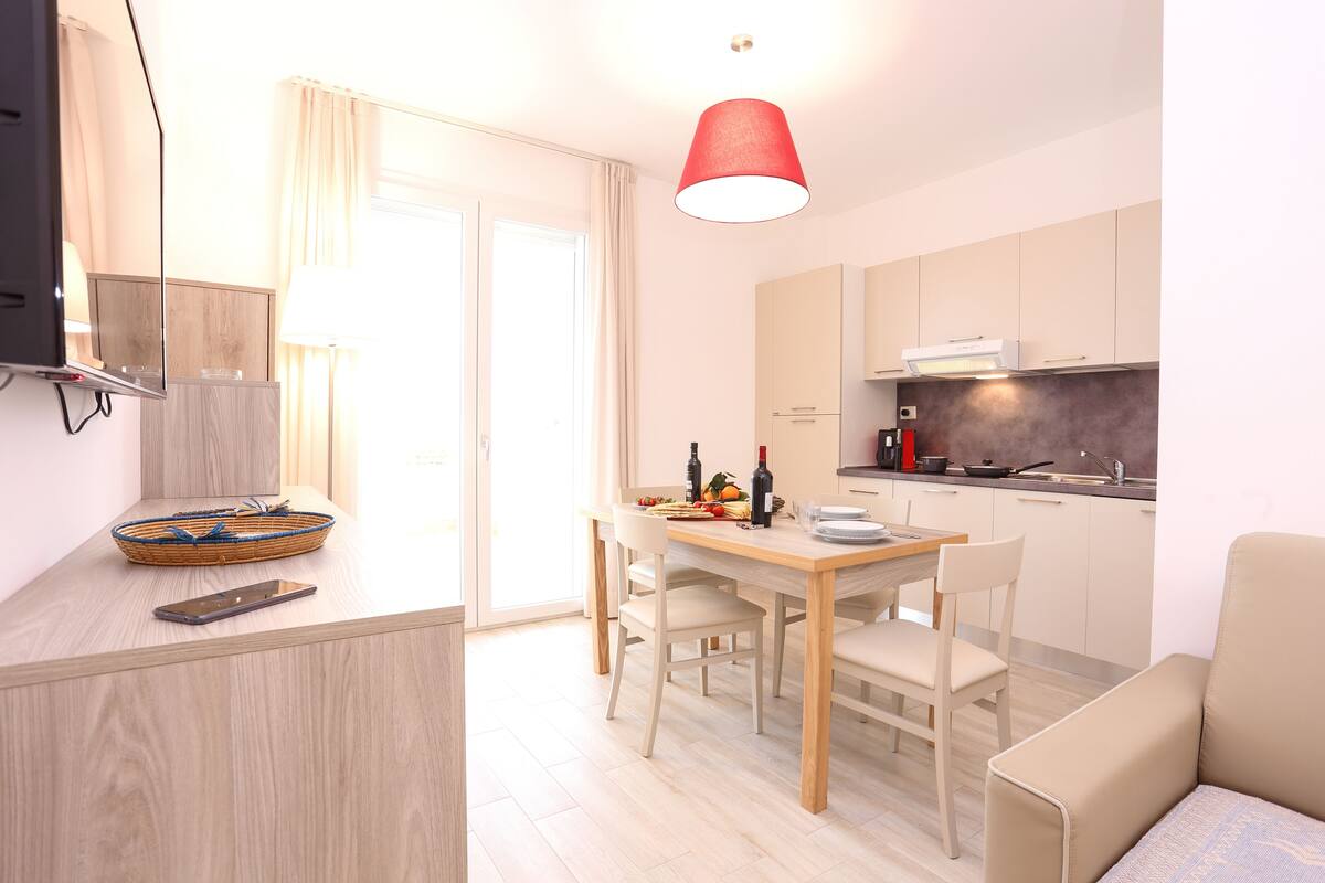 A modern kitchen with a dining area, a TV, and a red pendant light.