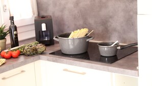 Una cocina con estufa, ollas, una botella, tomates y un alcachofa sobre la encimera.