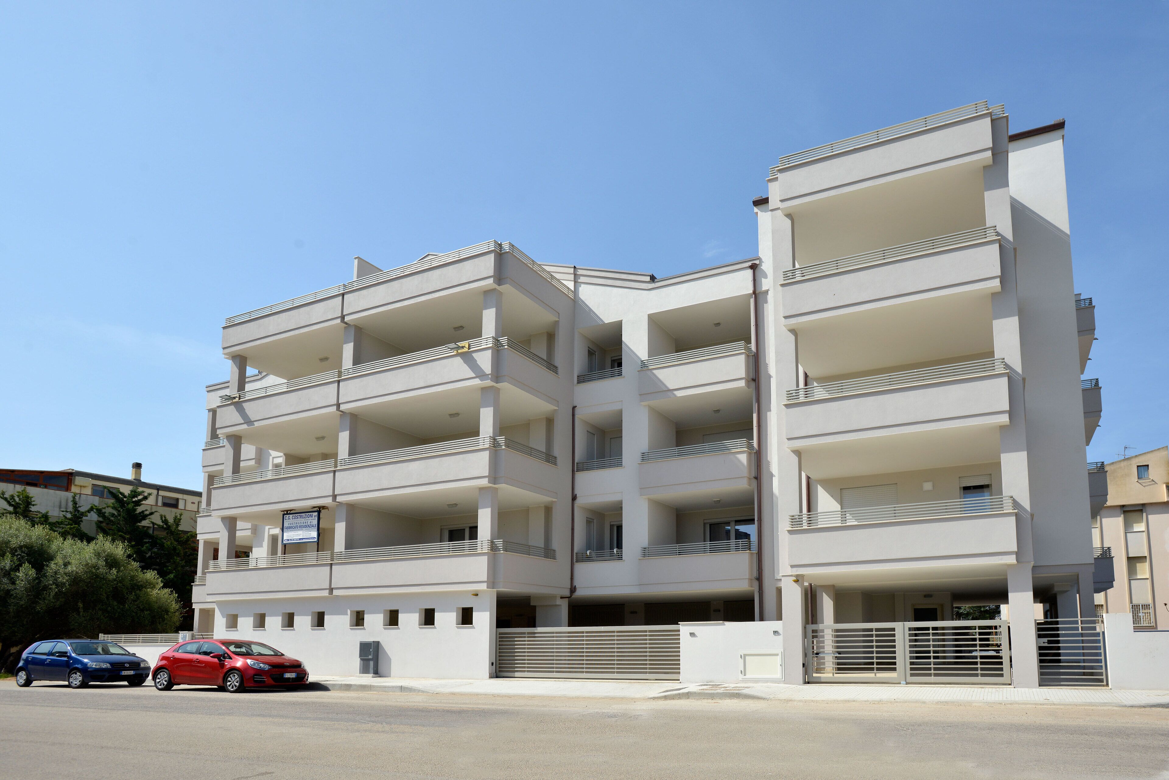 A multi-story residential building with balconies, a parking area, and a gated entrance.