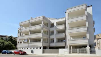 A multi-story residential building with balconies, a parking area, and a gated entrance.