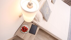 Una cama bien hecha con un cojín, una mesita de noche con una lámpara, un cuenco de fresas y una tableta.