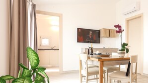 Una sala de estar moderna con comedor, televisor montado en la pared y una planta en maceta.