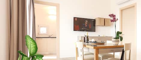 A modern living room with a dining area, a television mounted on the wall, and a potted plant.