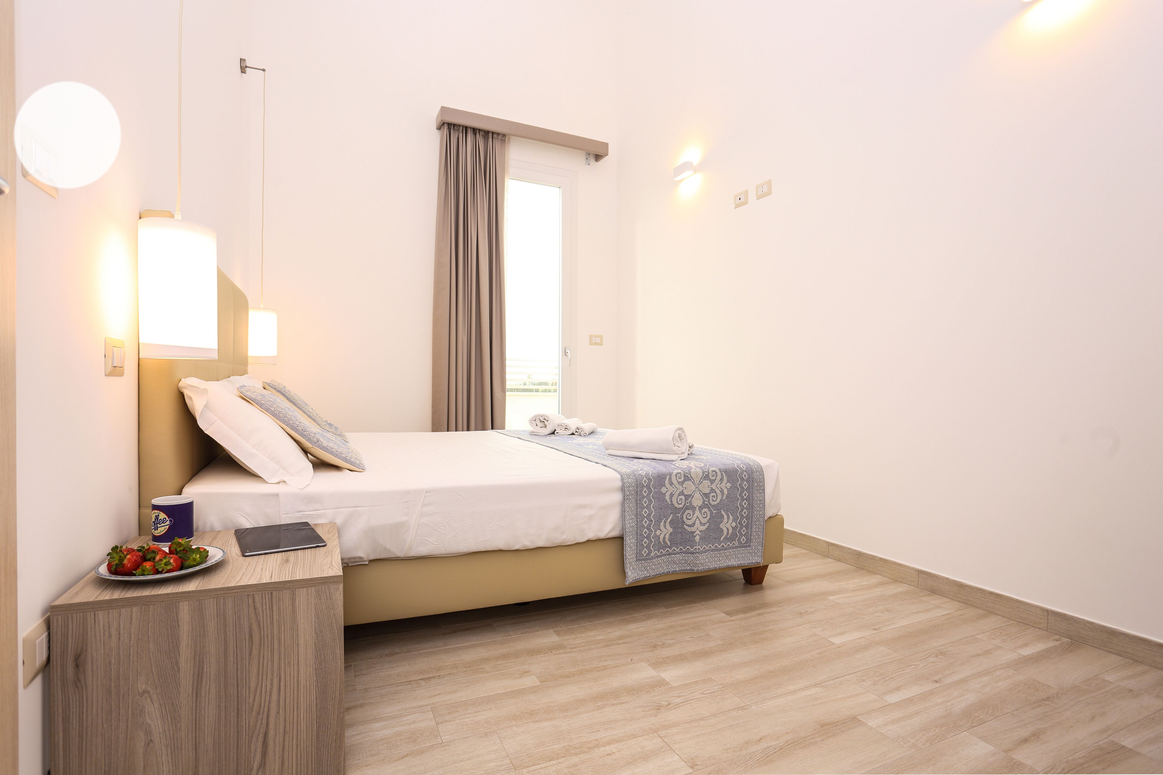 A hotel room with a bed, bedside table, and a window with curtains.
