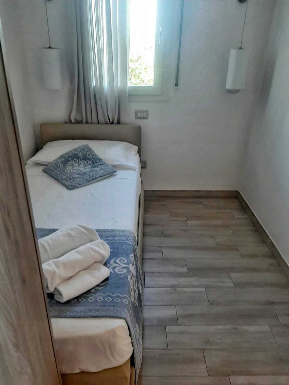 Une chambre à coucher avec un lit, une fenêtre avec des rideaux, un plancher en bois et deux lampes fixées au mur.