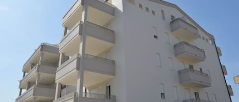 Een meerhoog gebouw met balkons, een plat dak en een heldere lucht.