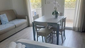 Habitación de hotel con cama, sofá, mesa de comedor con sillas y vistas a zonas verdes.